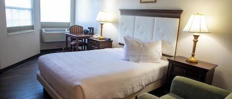 Quarto de hotel com uma cama grande, duas luminárias de cabeceira, uma escrivaninha com cadeira e uma janela com persianas.