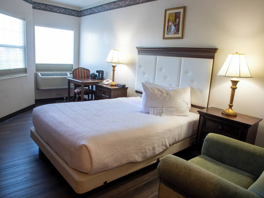 Habitación de hotel con una cama grande, dos lámparas de noche, un escritorio con una silla y una ventana con persianas.