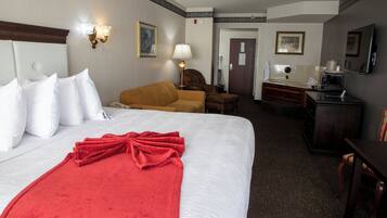 A hotel room with a large bed, a red blanket, a sofa, a desk with a chair, and a television.