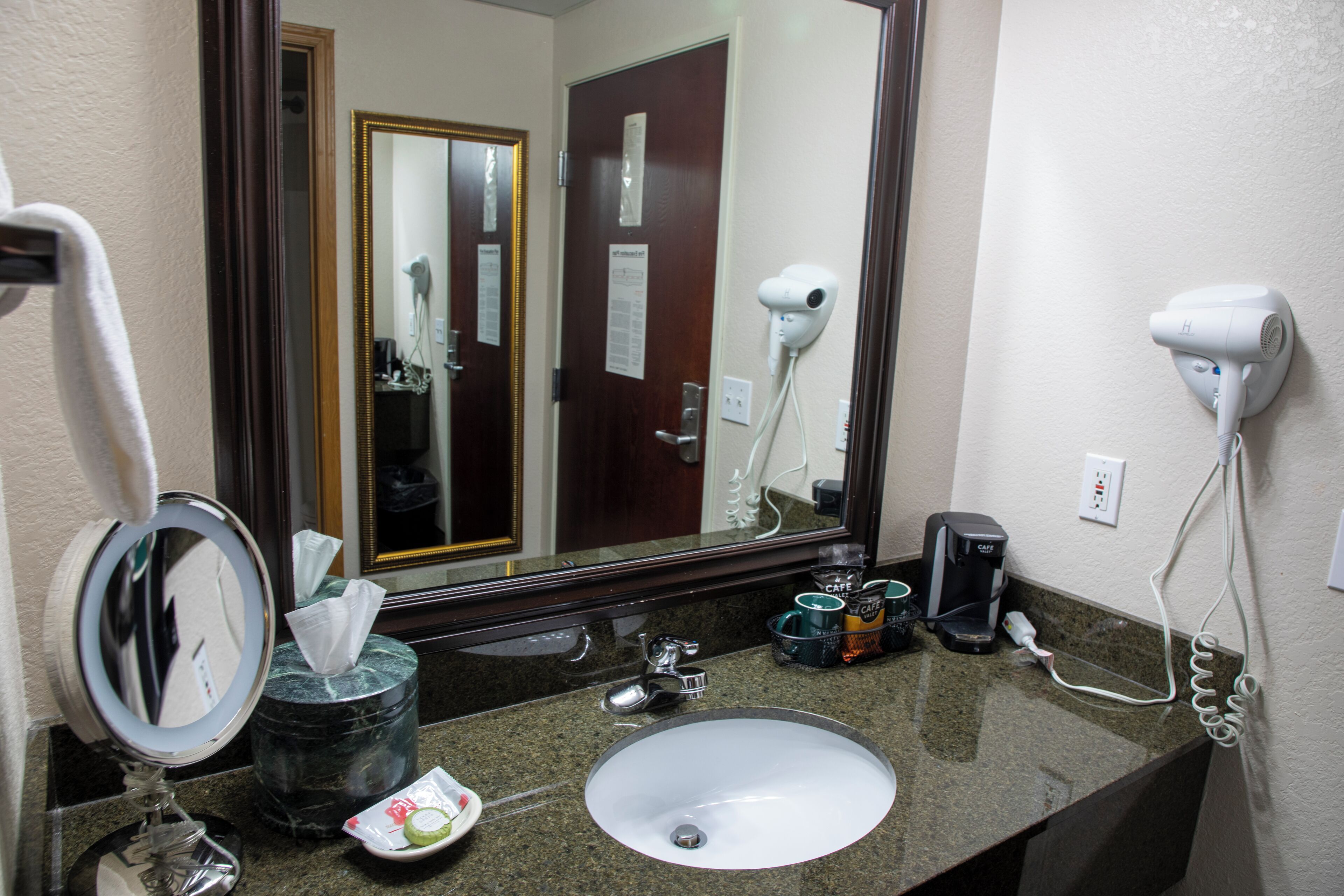 Une salle de bain d’hôtel équipée d’un lavabo, d’un miroir, d’un sèche-cheveux et d’une machine à café.