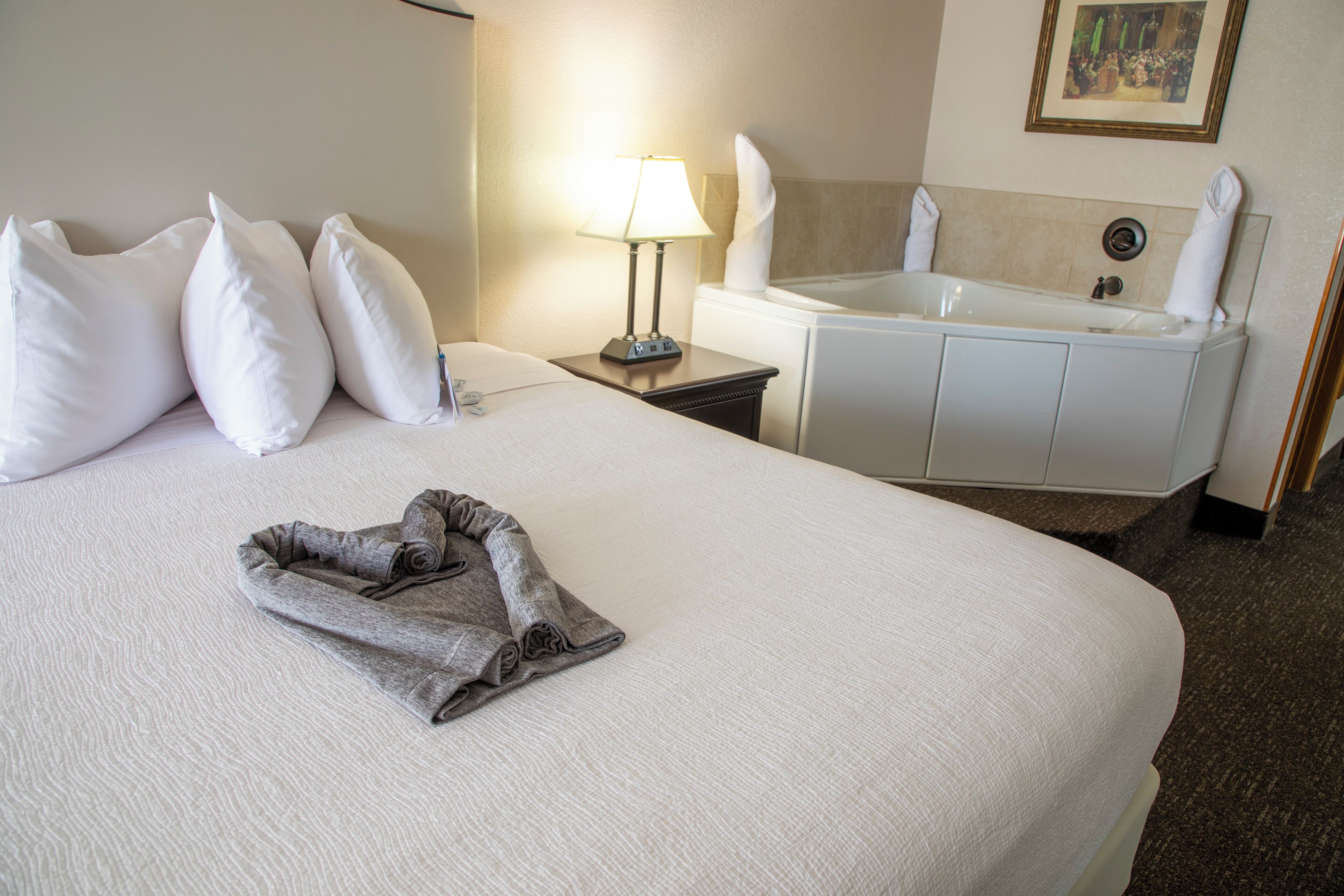 Quarto de hotel com cama arrumada, banheiro com banheira e toalha na cama.