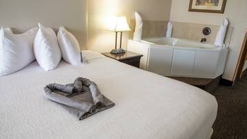 Quarto de hotel com cama arrumada, banheiro com banheira e toalha na cama.