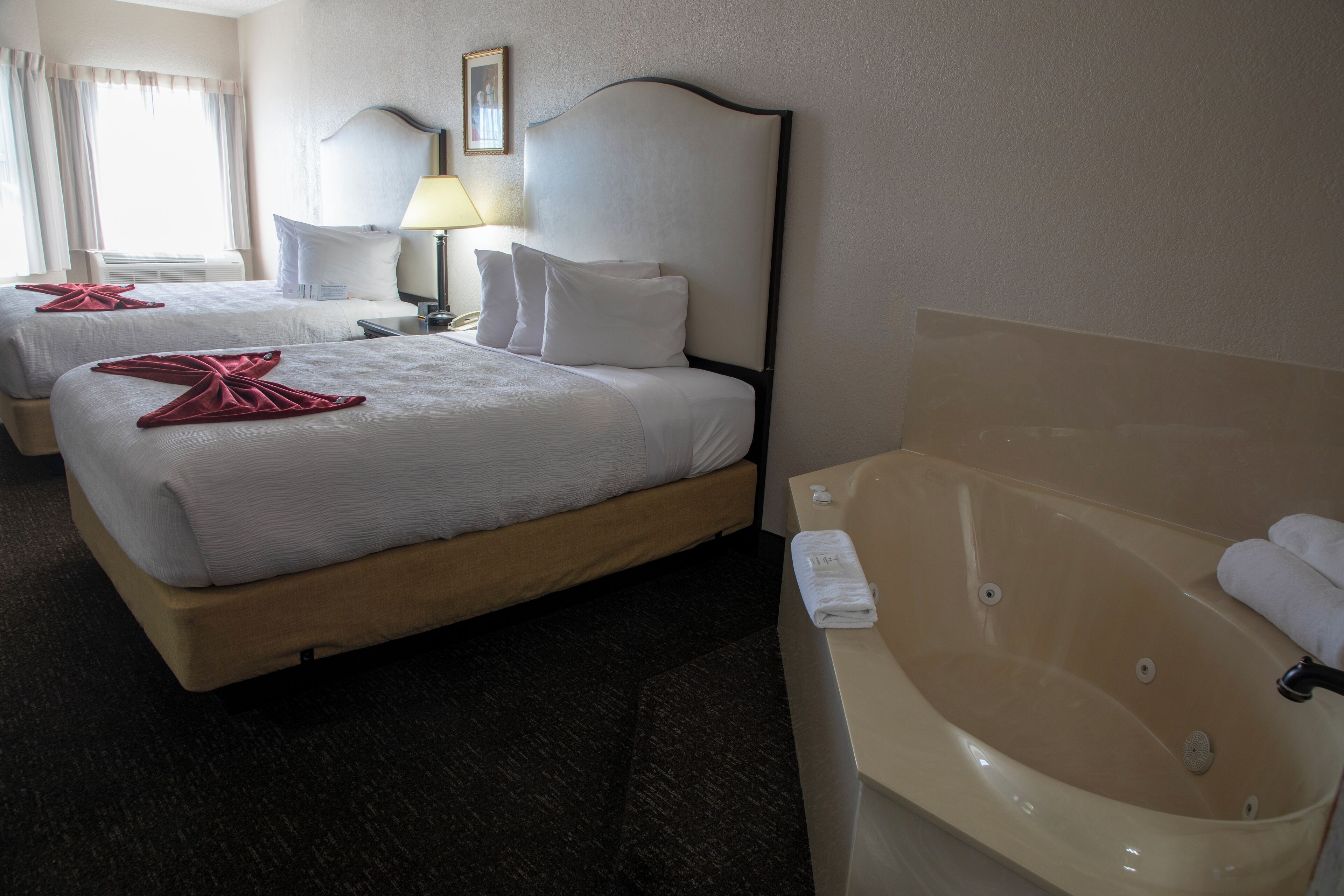 A hotel room with two beds, a large bathtub, and a window with curtains.