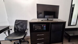 Habitación compacta con kitchenette, televisor de pantalla plana, una silla y una pequeña mesa.
