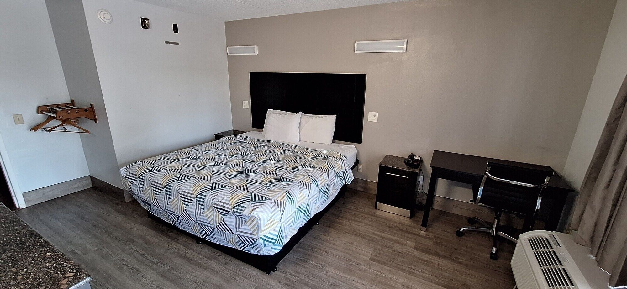 Een hotelkamer met een bed, een bureau, een stoel, een bijzettafeltje en een verwarming.