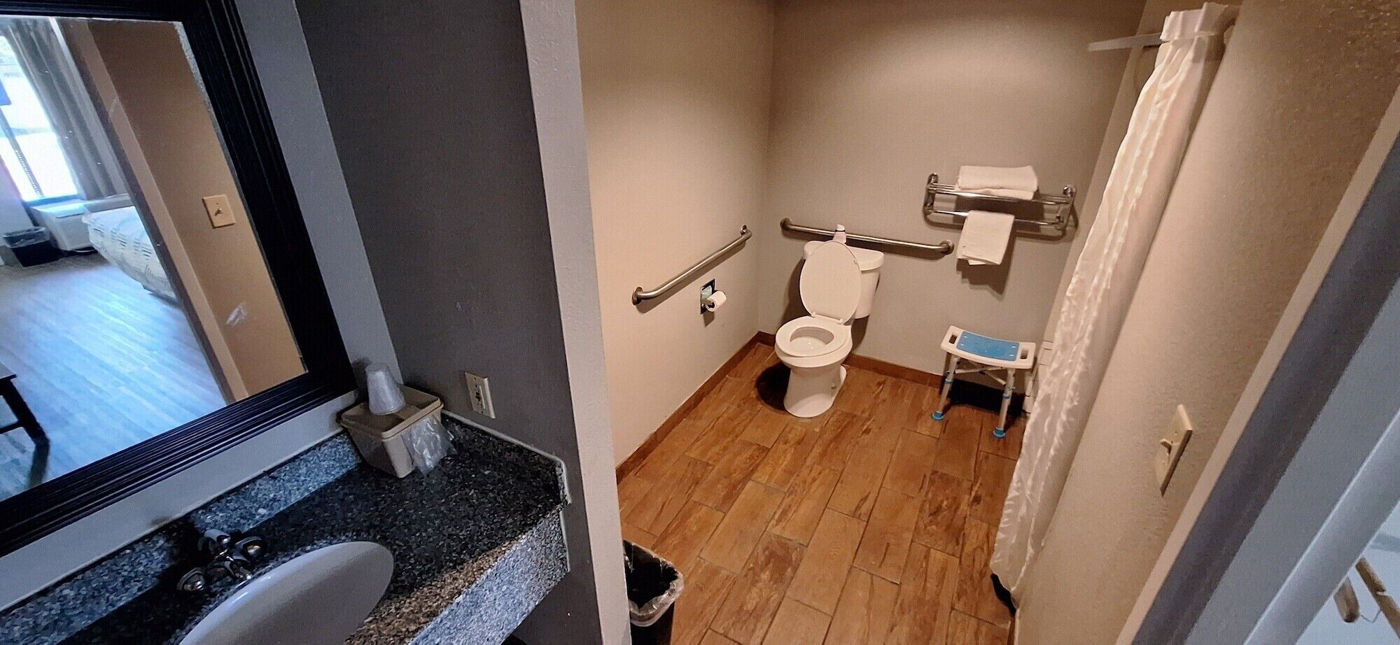Un baño con inodoro, barras de apoyo, un taburete pequeño y un perchero para toallas.