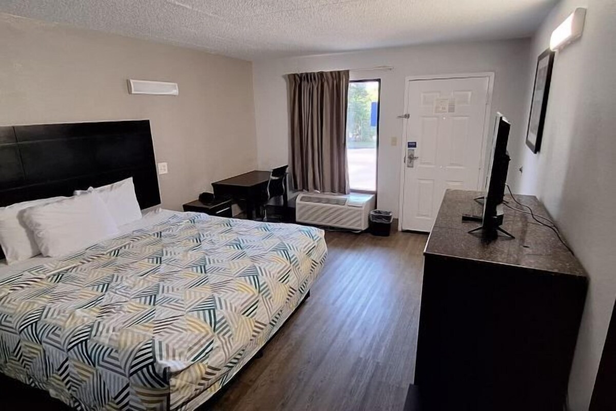 Een hotelkamer met een bed, een bureau, een stoel, een televisie en een deur naar een balkon.