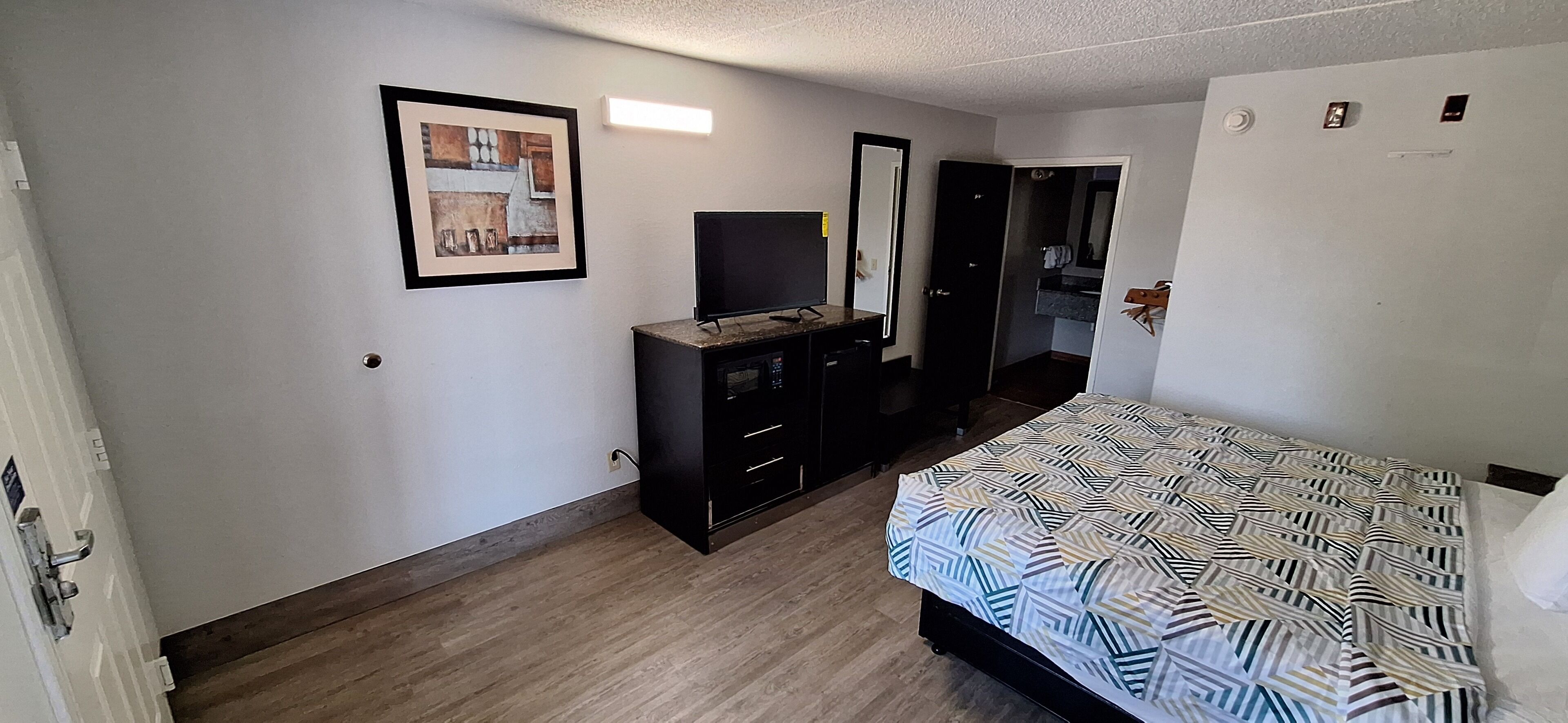 A bedroom with a bed, a dresser, a television, and a door leading to a bathroom.