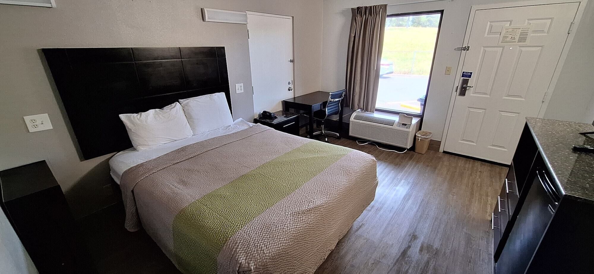 Una habitación de hotel con cama, escritorio, silla, radiador y puerta.