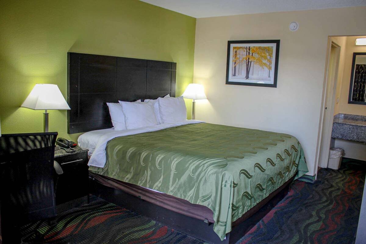 A hotel room with a bed, two bedside lamps, a desk with a telephone, and a framed picture on the wall.