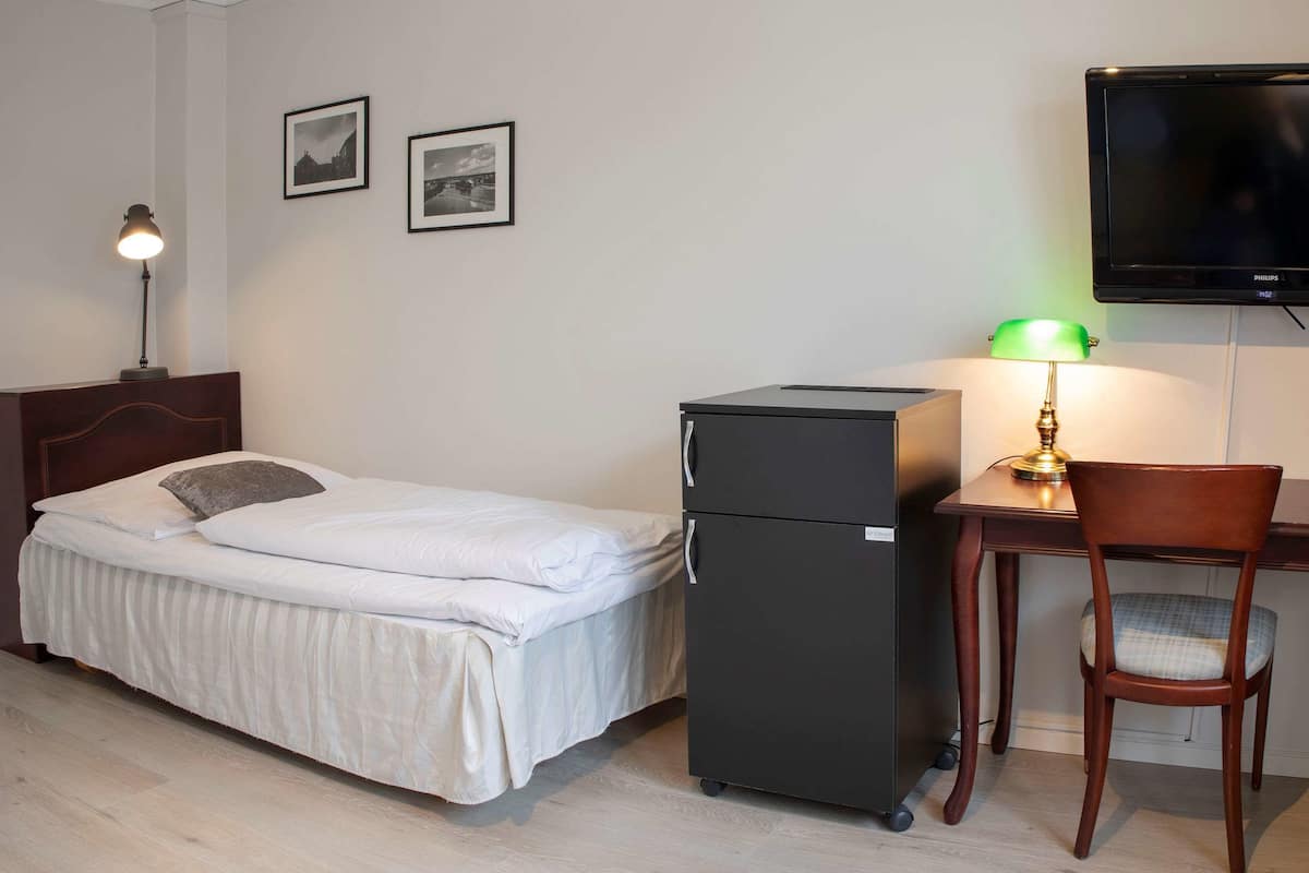 A bedroom with a bed, a desk with a chair, a television, and a refrigerator.