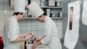 Un chef preparando comida en una cocina con paredes de azulejos y electrodomésticos de acero inoxidable.