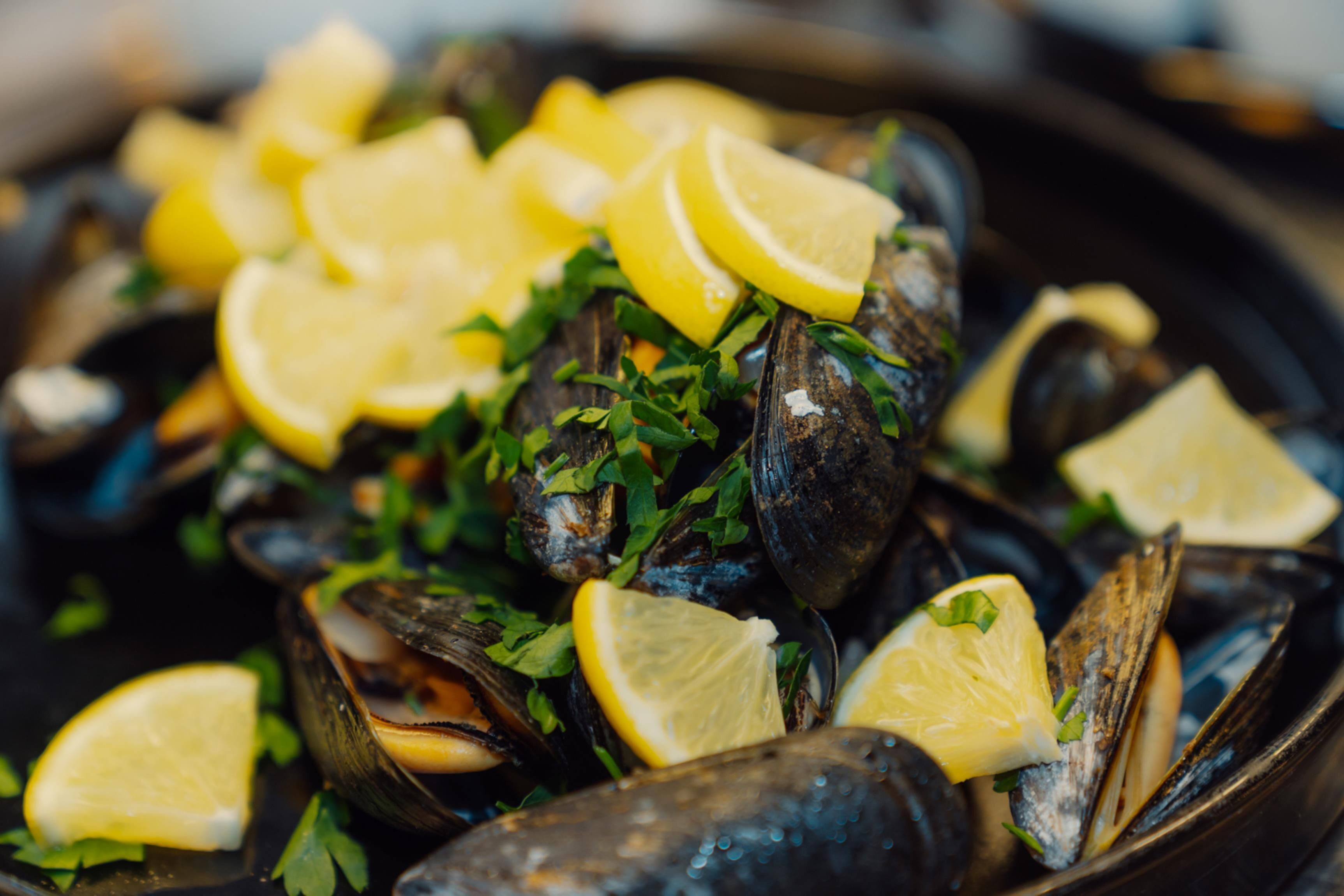 Primer plano de mejillones adornados con rodajas de limón y perejil picado.