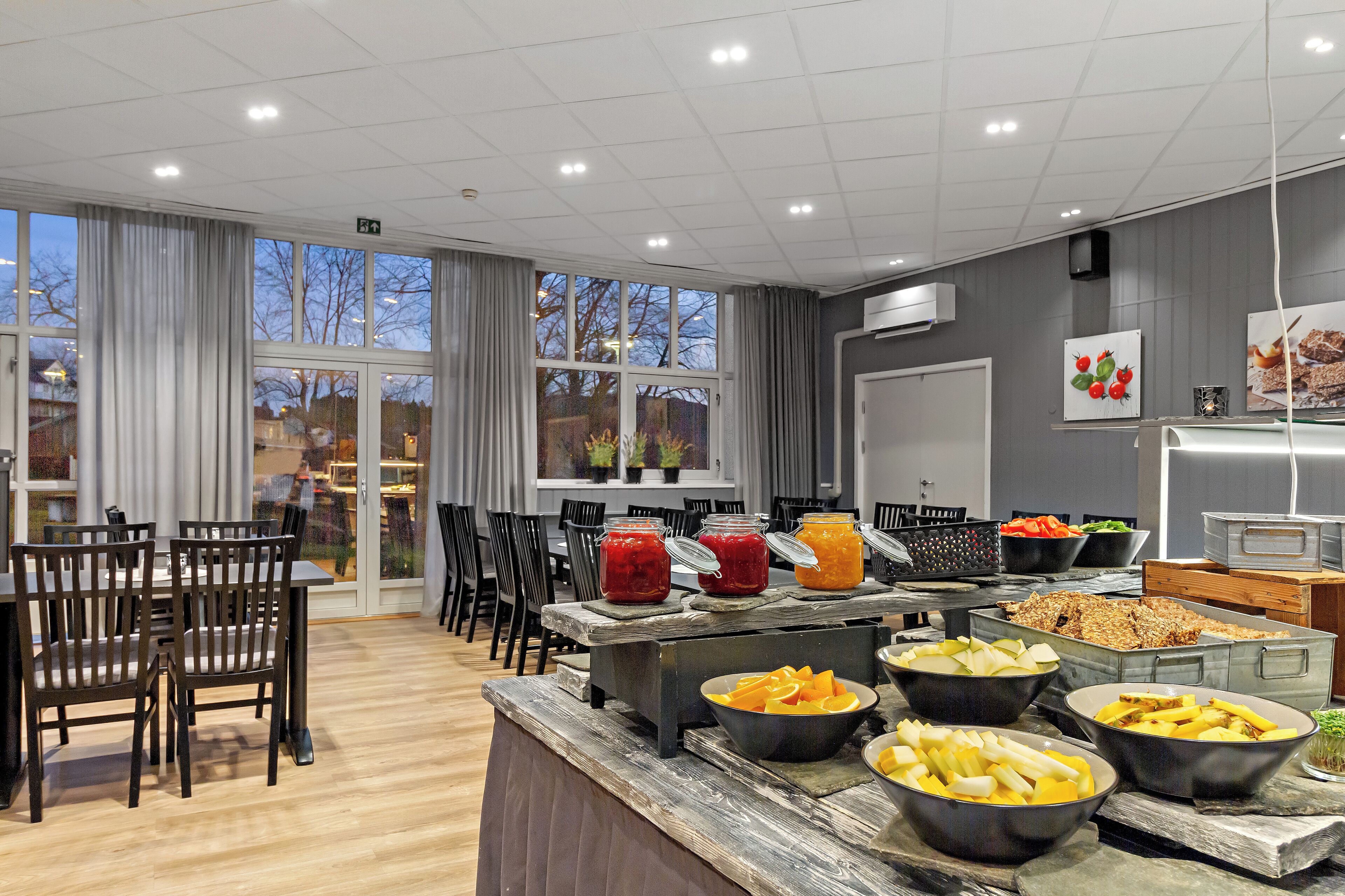 A buffet setup with various food items, a dining area with chairs, and a view of the outside through large windows.