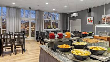 A buffet setup with various food items, a dining area with chairs, and a view of the outside through large windows.