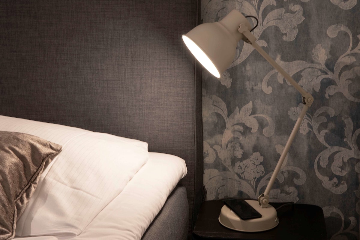 A neatly made bed with a pillow, a bedside lamp, and a smartphone on a nightstand.