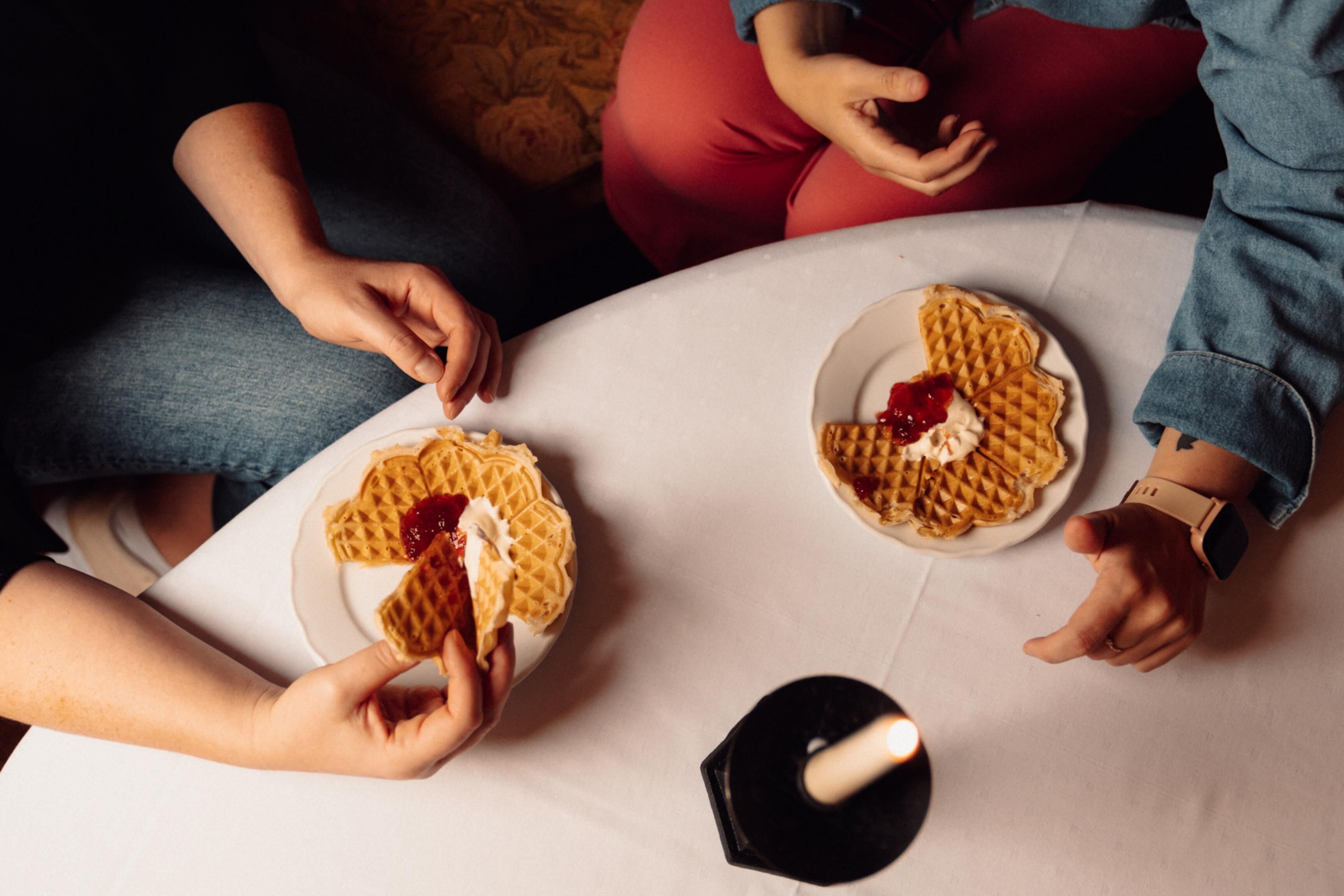 A group of people sitting around a table with waffles and jam.