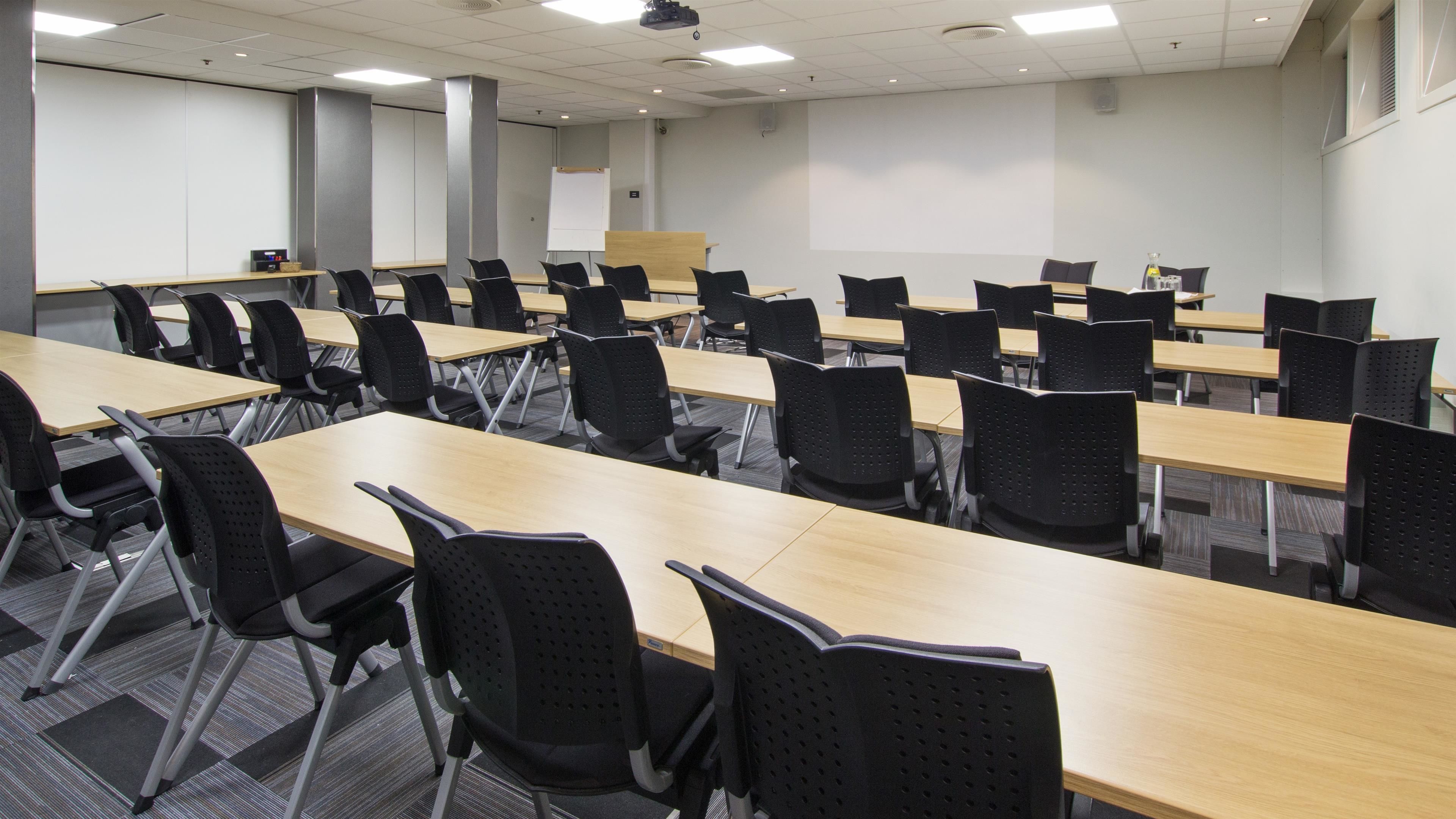 Ein Konferenzraum mit mehreren Tischen, Stühlen, einer Whiteboard-Tafel und einer Projektionsleinwand.