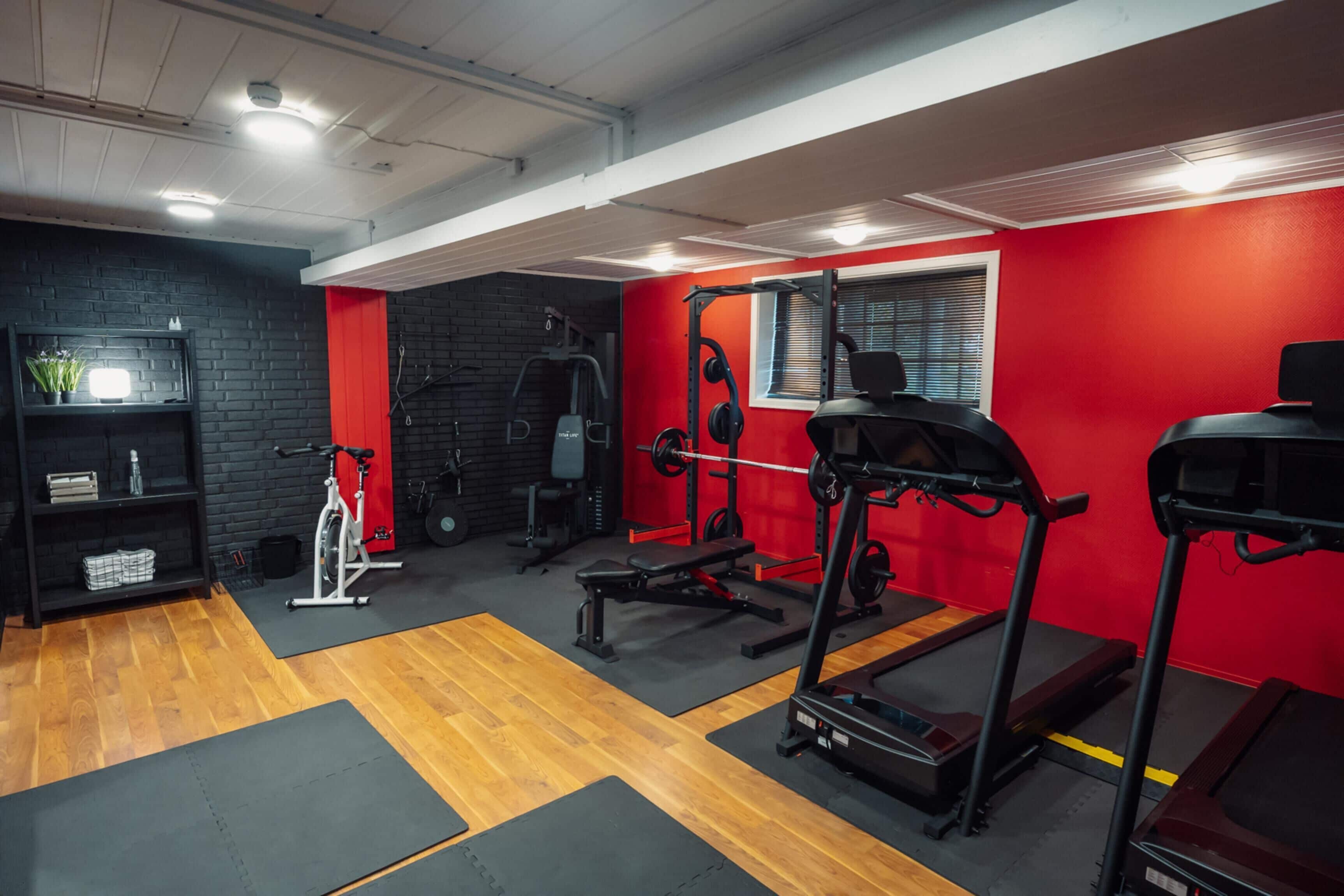 A gym with exercise equipment, wooden flooring, and a red accent wall.