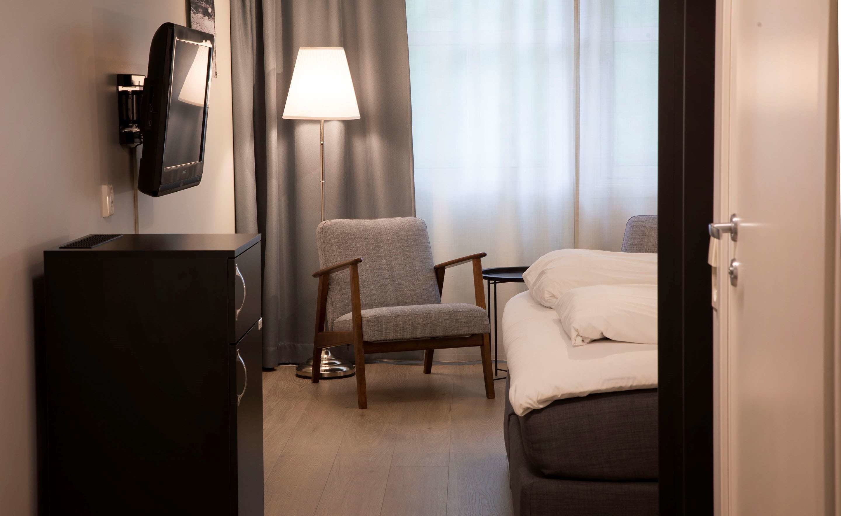 Una habitación de hotel con una cama, una silla, un escritorio, una lámpara y un televisor montado en la pared.