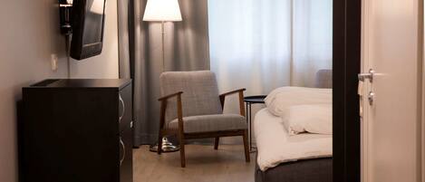 Una habitación de hotel con una cama, una silla, un escritorio, una lámpara y un televisor montado en la pared.
