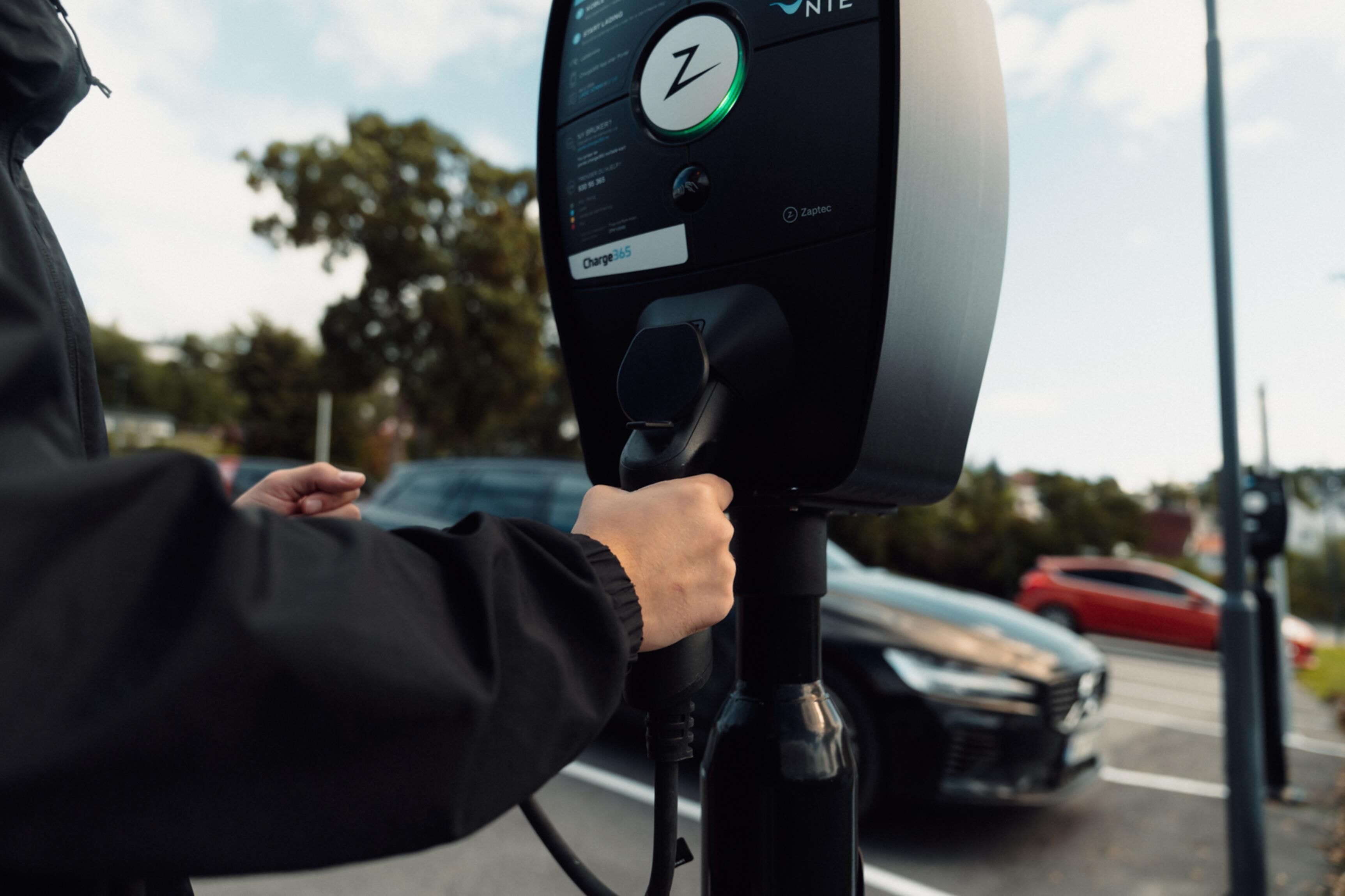 A person plugging a charging cable into a ZAPTEC Charge 365 electric vehicle charging station.