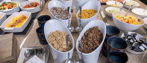 A buffet with various food items in white bowls and trays, including fruits, vegetables, and cereals.
