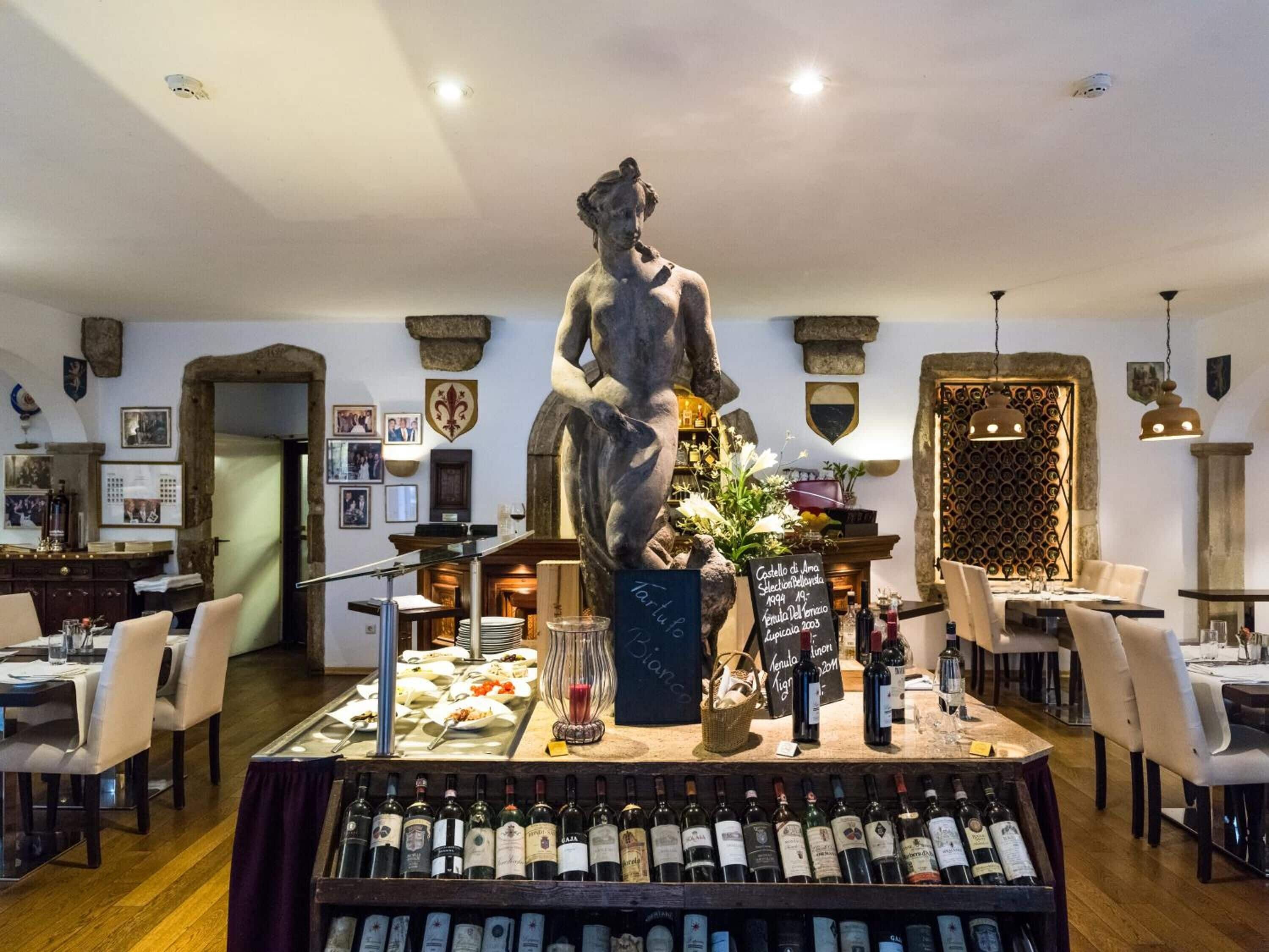 A restaurant interior with a central statue, a wine display, and a dining area with tables and chairs.