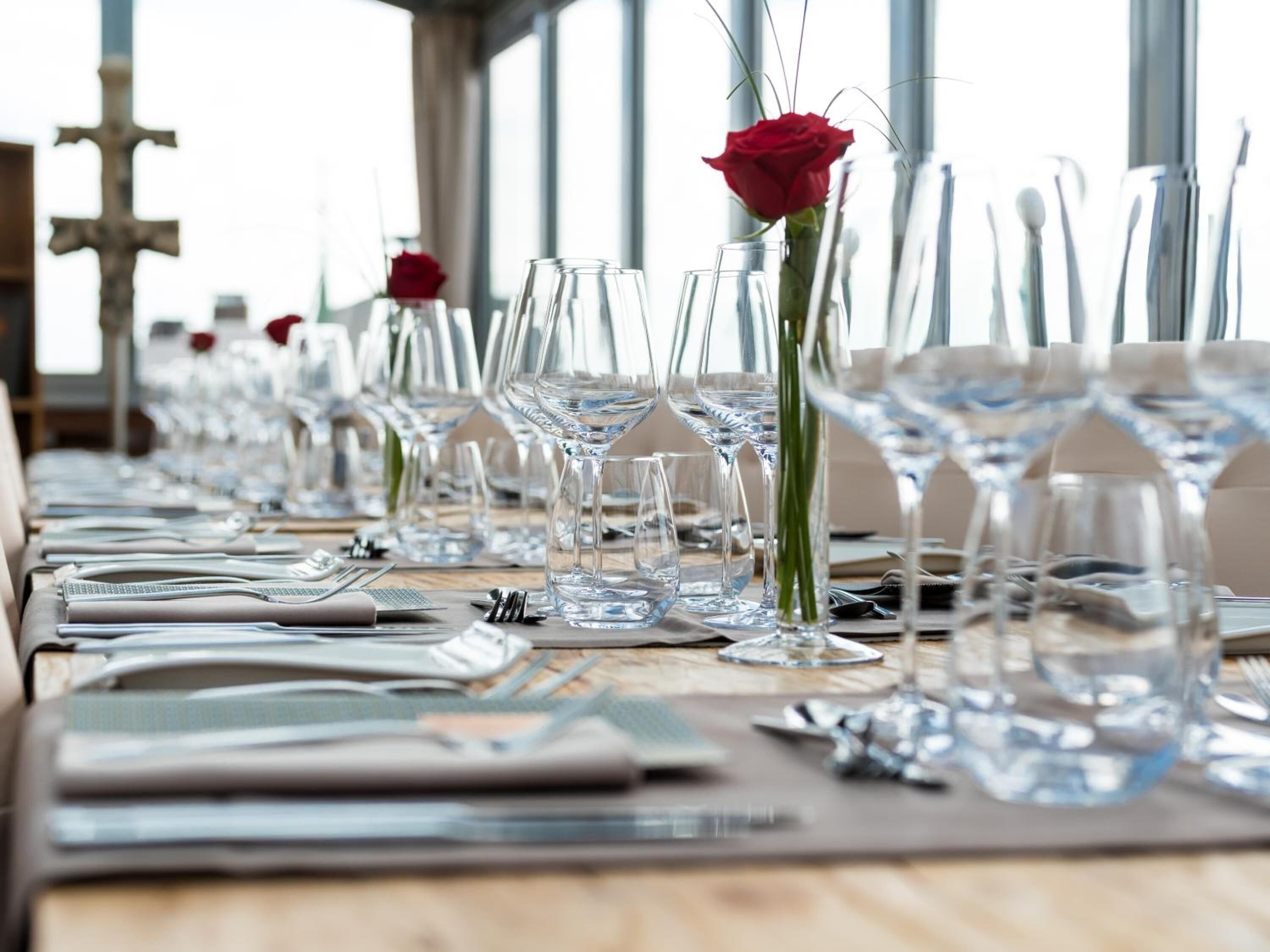 A long table set for dining with multiple wine glasses and rose vases.