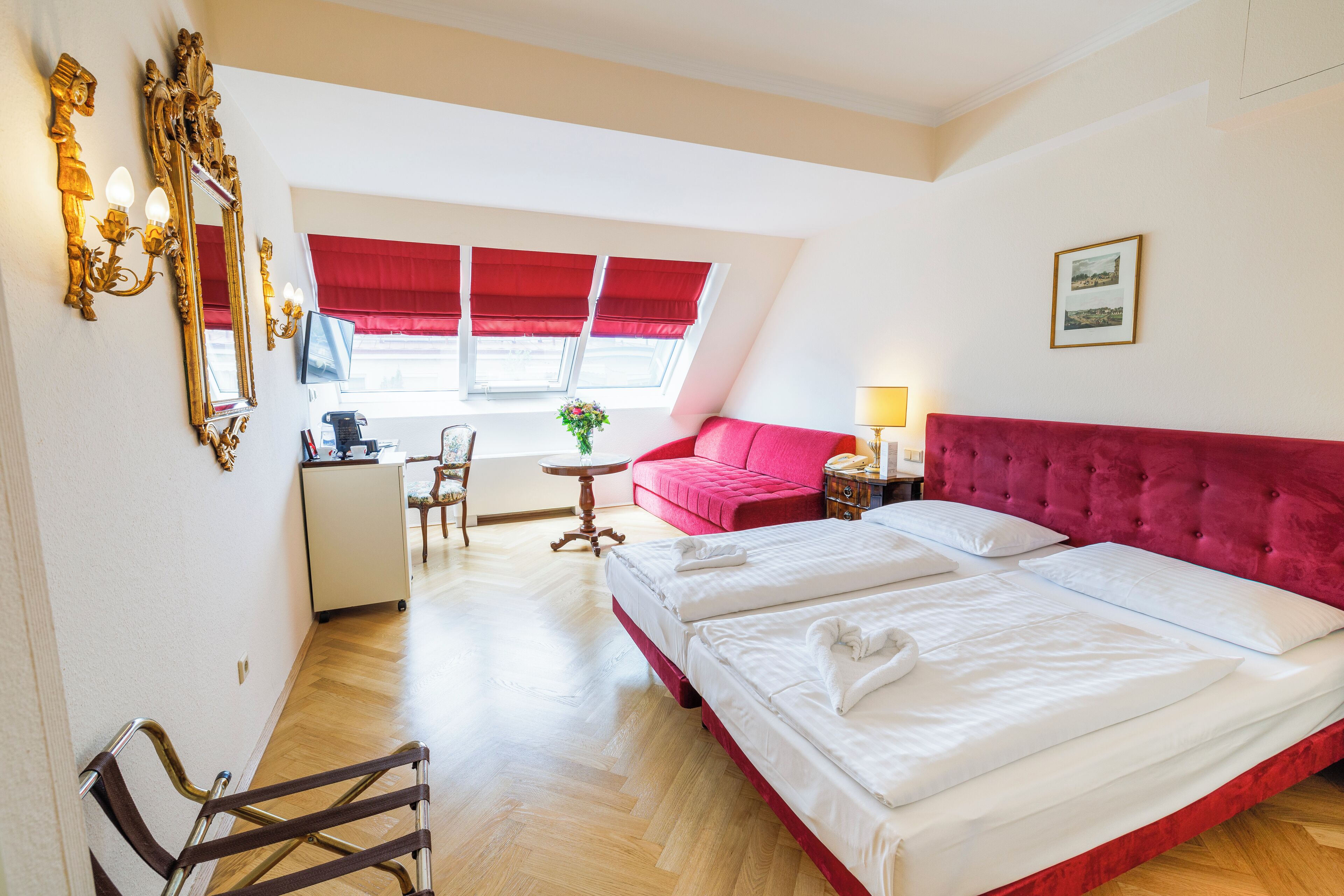 A hotel room with a large bed, a desk, a chair, and a red sofa.