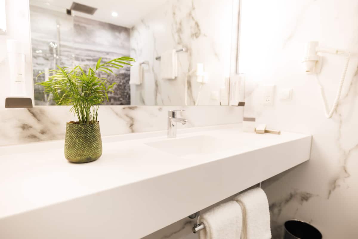A bathroom with a white marble sink, a green plant in a textured pot, and a towel hanging on a rack.