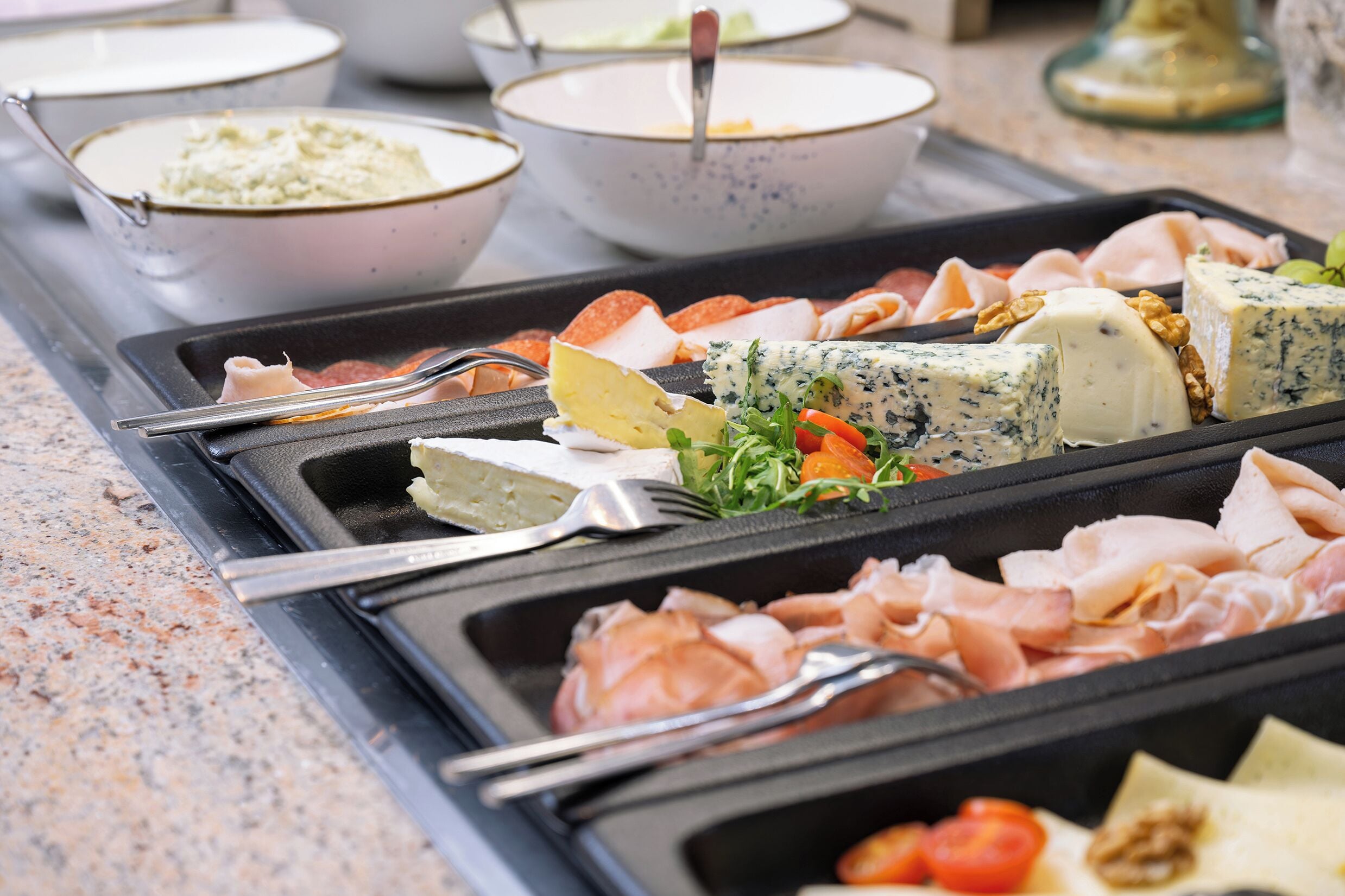 A buffet with various meats, cheeses, and vegetables.