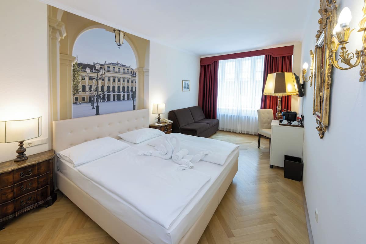 A hotel room with a large bed, a desk, a chair, a lamp, and a mirror.