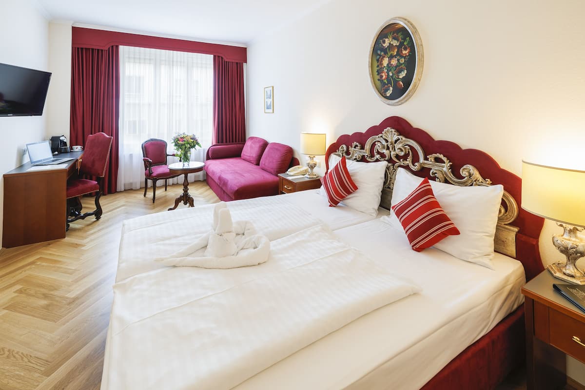 A hotel room with a large bed, a desk with a laptop, a chair, and a television on the wall.