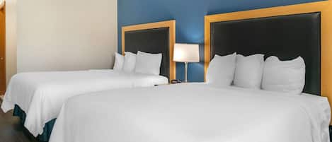 A hotel room with two single beds, a nightstand with a lamp, and a wooden headboard.