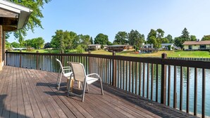 Une terrasse en bois avec deux chaises, donnant sur une étendue d’eau, entourée d’une clôture et bordée, au loin, par des immeubles d’habitation.