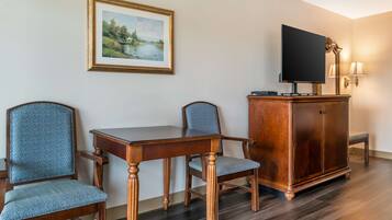 A room with a wooden dining table, two chairs, a cabinet with a flat-screen TV, and a framed painting on the wall.