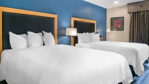 Une chambre d’hôtel avec deux lits, chacun doté d’une tête de lit en bois et de linge de lit blanc. Une lampe est fixée au mur entre les deux lits, et un tableau encadré orne le mur.