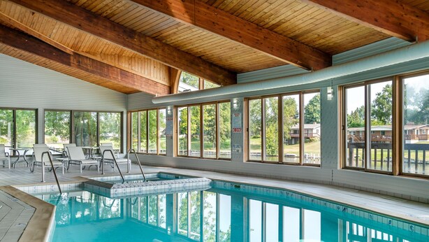 Une piscine intérieure offrant une vue dégagée sur les environs, avec des poutres en bois au plafond et un espace détente aménagé au bord de la piscine.