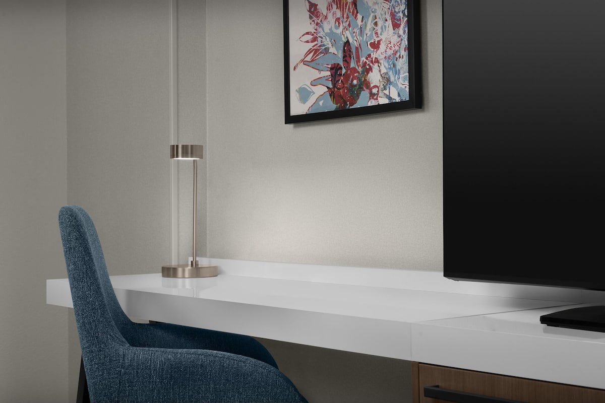 A modern office desk with a chair, a framed abstract painting, and a flat-screen TV.