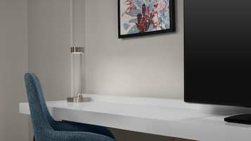 A modern office desk with a chair, a framed abstract painting, and a flat-screen TV.