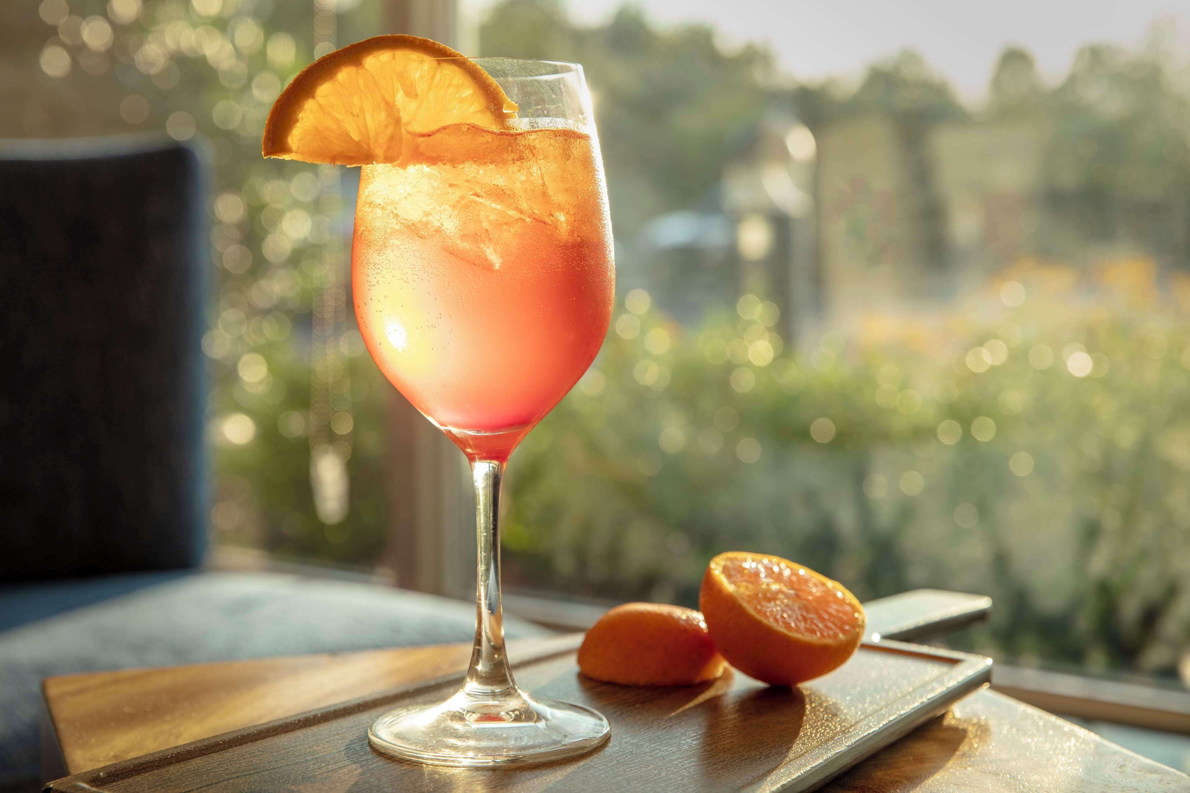 A cocktail glass with a slice of orange on the rim, placed on a wooden tray.
