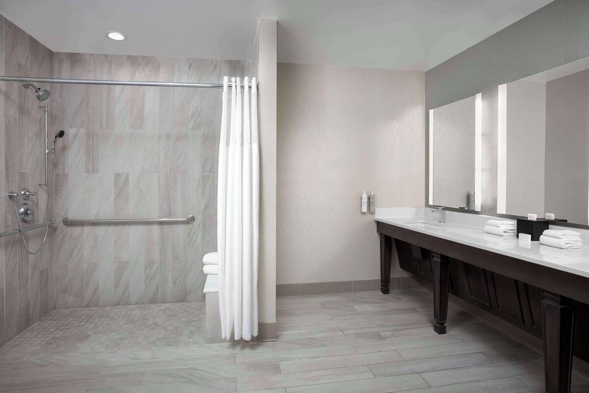 A modern bathroom with a walk-in shower, a vanity with a large mirror, and a tiled floor.