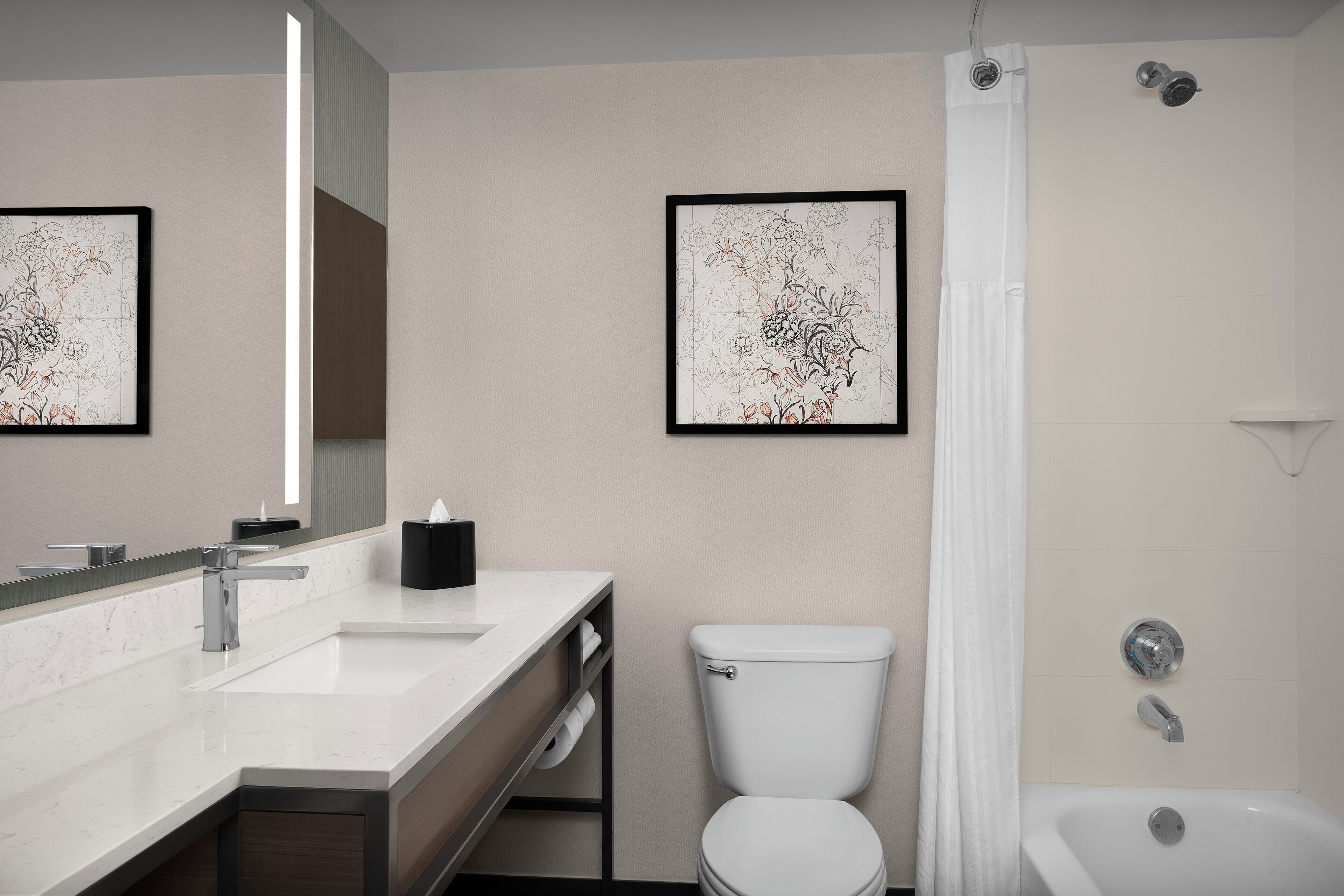 Une salle de bain moderne avec un lavabo, des toilettes et une baignoire, tous de couleur blanche. Les murs sont ornés d’œuvres d’art florales encadrées.
