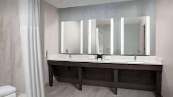A modern bathroom with a double sink vanity, a large mirror, and a shower area.