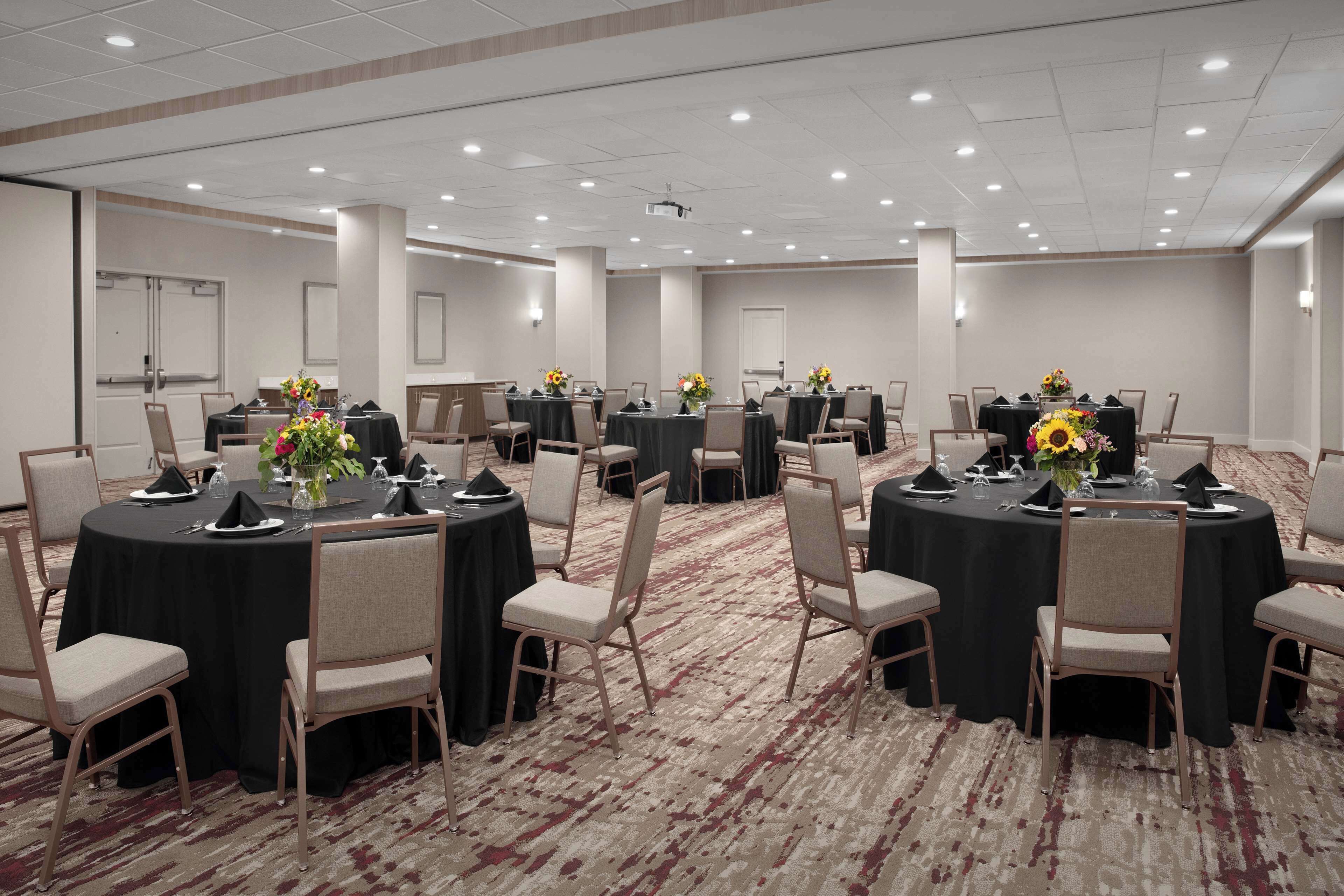 A conference room with multiple round tables, each set with chairs, laptops, and floral centerpieces.