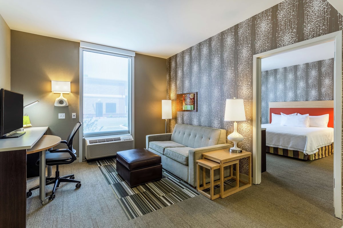 A hotel room with a desk, chair, sofa, ottoman, bedside tables, and a bed.