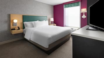 Een hotelkamer met een bed, nachtkastje, lamp en een televisie.
