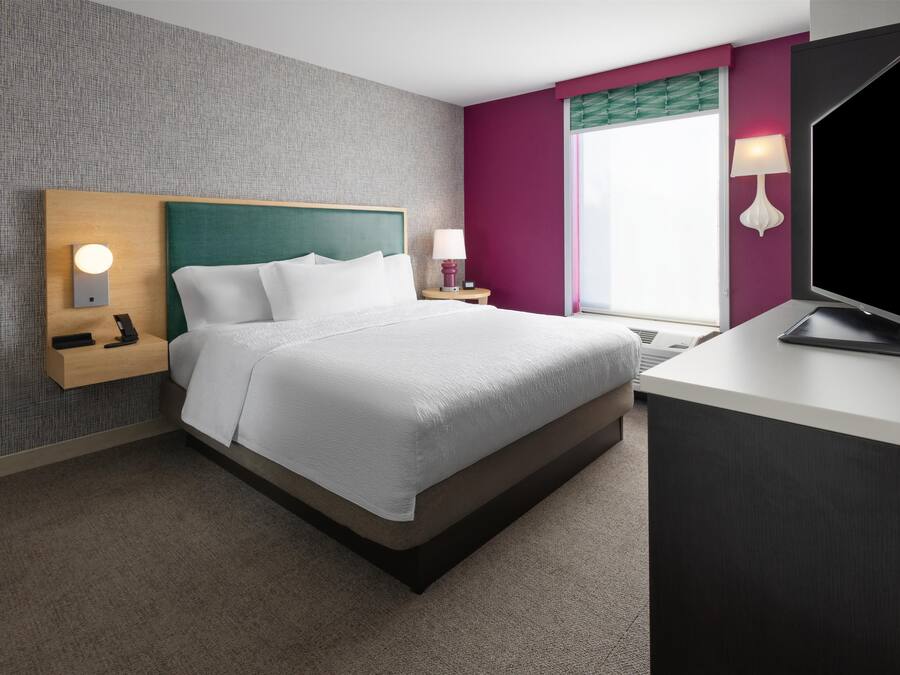 Een hotelkamer met een bed, nachtkastje, lamp en een televisie.