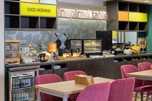 A breakfast area with waffle makers, a coffee machine, and a variety of food items on display. - Home2 Suites by Hilton Dover, DE (Dover)